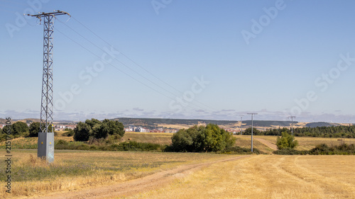 Photography Torre eléctrica en campo rural con camino bajo cielo azul