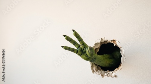 Green Monster Hand Emerging from Hole in White Wall