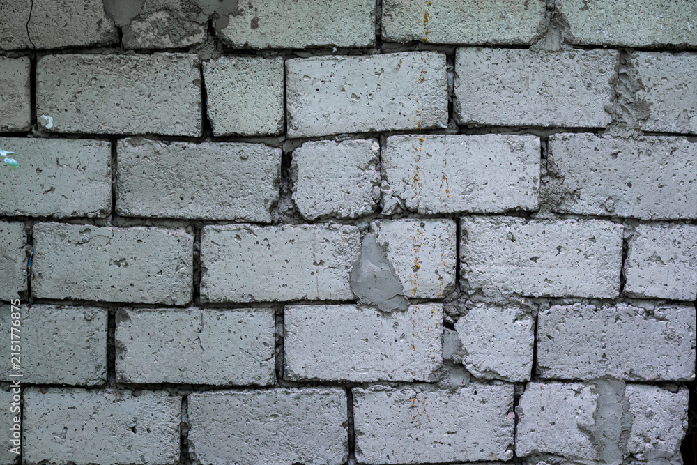 Obraz premium A wall of gray concrete blocks bonded with cement with large gaps. The surface is uneven and rough, with exposed cement mortar.