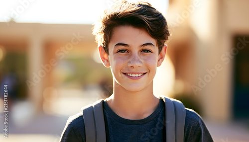 A cheerful smiling middle school boy with a backpack is featured in the portrait