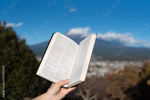 Outdoors, an open Bible showing Jeremiah chapter 9 is held by a hand against Mount Fuji and Fujinomiya city from Shirao Mountain Park (Shiraosan). Horizontal shot.