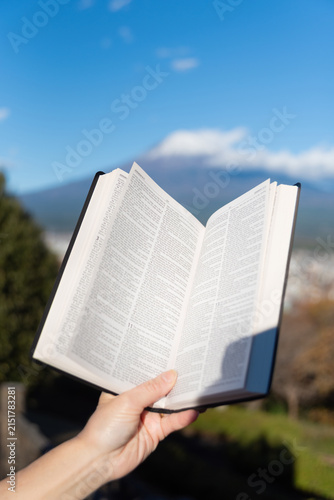 Outdoors, an open Bible showing Jeremiah chapter 9 is held by a hand against Mount Fuji and Fujinomiya city from Shirao Mountain Park (Shiraosan). Vertical shot.