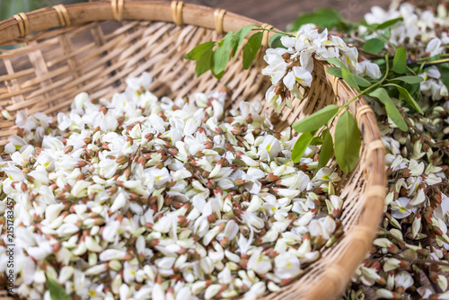 Fotografía Fresh white locust blossoms with green leaves fill a woven bamboo basket, showcasing natural seasonal produce