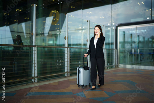 Businesswoman on commute transit talking on the smartphone while walking with hand luggage in airpot going to boarding gate. Asian woman happy using mobile phone app for conversation