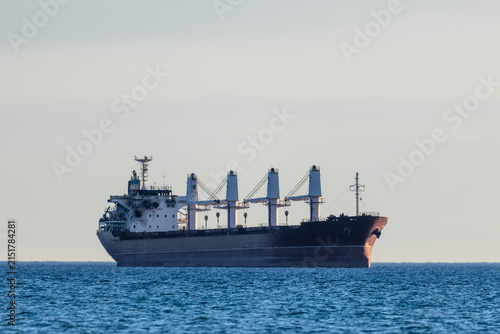 A large cargo ship with deck cranes with a damaged wheelhouse as a result of a drone attack, standing on calm open water, side view