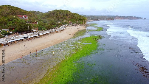 Fotografie Aerial drone view of people walking on vibrant green mossy coral reef at a tropical beach