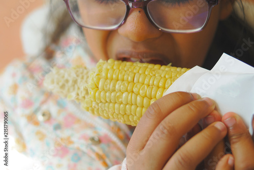 Obraz na płótnie Girl eats corn on the cob while holding it in her hands