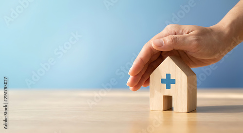 Hand shielding miniature wooden house with medical cross for health and property insurance concept
