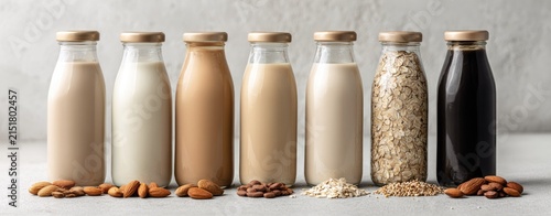 Various plant-based milks in glass bottles, accompanied by their source ingredients