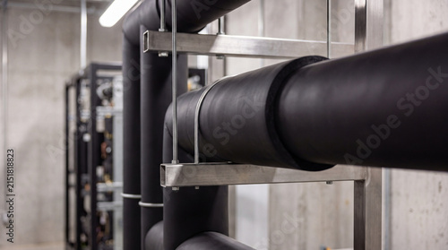 Fotografie Detailed close-up photograph of robust black insulated pipes securely supported by sturdy metal brackets in a modern