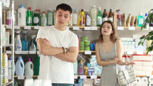 Young woman stands in a supermarket upset and resentful of a man who is standing in the background and talking emotionally. Couple quarrels in the hardware store