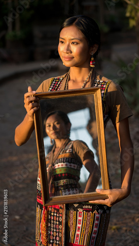 Woman holding a mirror reflecting her face, outdoors in traditional attire.