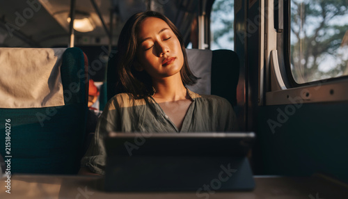 Woman sleeping on a train using a tablet device.