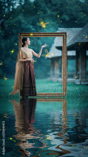 Woman standing near water with butterflies and glowing fireflies in a surreal scene.