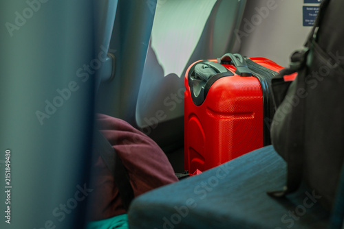 A red carry-on suitcase and other personal luggage rest on the floor between passenger seats inside a train or bus, captured in a candid, travel-focused interior photo.
