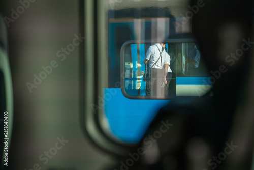 A reflection in a train window shows uniformed railway staff standing outside on a station platform, framed through an interior perspective inside a passenger carriage.