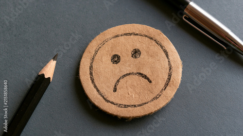 Sad smiley face drawn on wooden token with pencils negative depression melancholy expression conceptual psychology pessimism disappointment sorrowful reaction