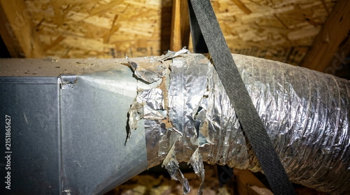 HVAC ductwork with torn insulation and deteriorating flexible duct in dusty residential attic, home inspection and repair concept.