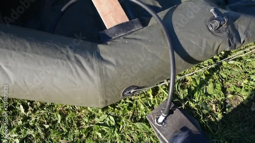 Man inflating a green rubber boat using a foot pump. Person pumping air into a vessel on the grass. Equipment setup for water recreation and outdoor activity.