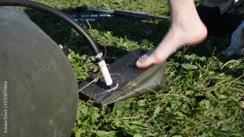 Woman using foot pump to inflate rubber boat on green grass. Active person prepares equipment for water travel. Outdoor activity and camping preparation concept.