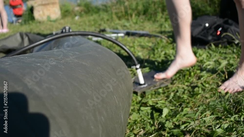 Woman inflating a rubber raft with a foot pump on grass. Person preparing equipment for outdoor water activity. Leisure recreation and nature travel concept.