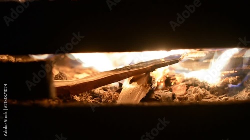 Glowing wood burning in a fireplace. Intense orange flames flicker over dry logs and hot embers. Domestic heating scene showcasing energy and cozy home interior.