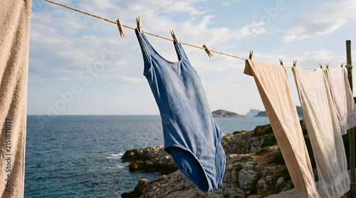 Blue swimsuit hanging on clothesline with sea and sky background.
