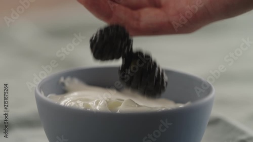 Slow motion man hand add ripe blackberries to yogurt in a bowl