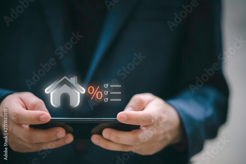 Businessman using telephone and laptop with house interest rate icon. Concept of real estate tax, mortgage loan calculation, financial planning, and home property investment.