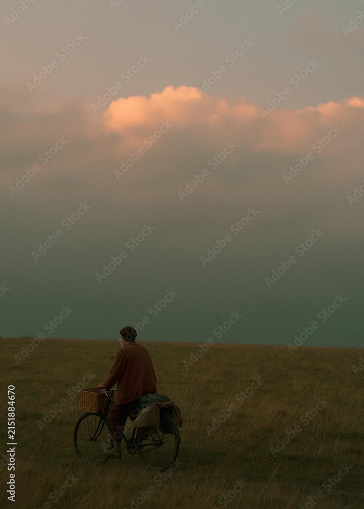 Fototapeta premium Man riding a bicycle on a grassy field. he is wearing a brown jacket and a cap, and has a basket attached to the back of the bicycle.