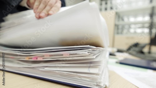 Thick stack of white document pages lies on office desk. Blue folder cover protects heavy archive files from dust damage. Office paperwork