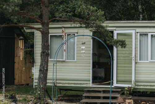 Photography Mobile home with green exterior and white windows surrounded by trees, featuring