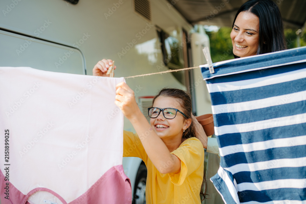 Obraz premium Mother and daughter hanging laundry beside camper on family vacation.
