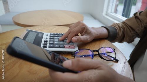 Professional business and financial planning concept featuring an entrepreneur working with a laptop, calculator, smartphone, and digital tablet at a wooden desk