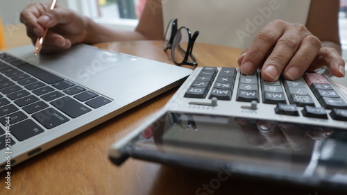 Professional business and financial planning concept featuring an entrepreneur working with a laptop, calculator, smartphone, and digital tablet at a wooden desk