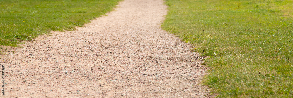 Obraz premium Gravel footpath walkway leading through green grass field in park background