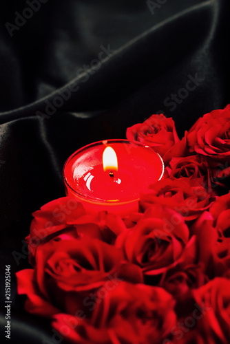 Foto Red roses surround a lit candle on a dark fabric