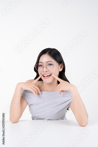 Cheerful young Asian woman smiling with fingers touching cheek and wearing glasses on white background.