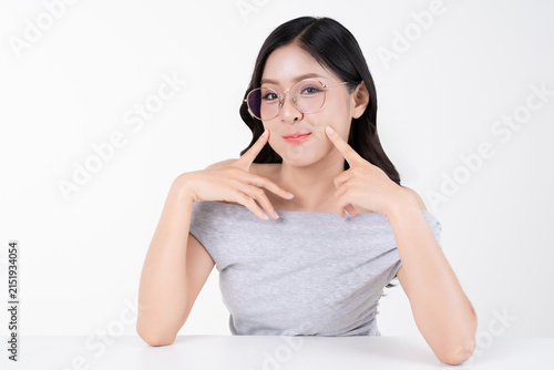 Cute young Asian woman thinking with fingers touching cheek and wearing glasses on white background.