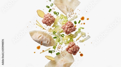 Dumplings with minced pork filling, cabbage, sliced ginger, and green onions appear to levitate in mid-air to illustrate the careful preparation of classic Asian appetizers.