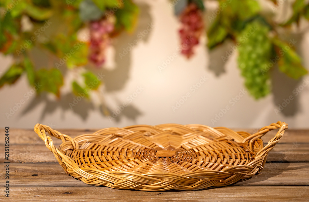 Obraz premium Wicker basket on wooden table with blurred grape leaves for rustic autumn harvest product scene