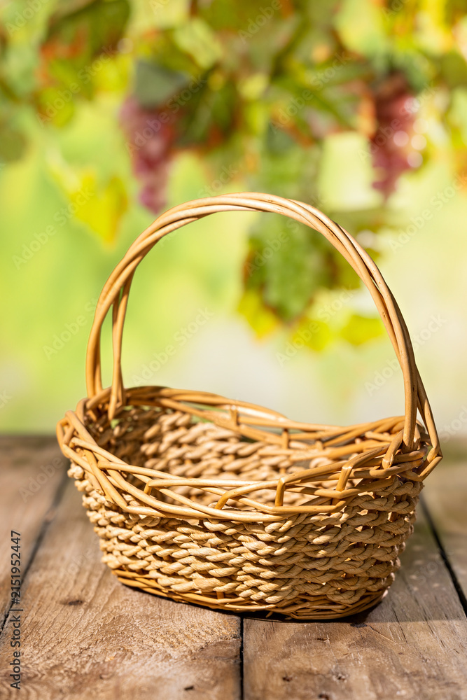 Obraz premium Empty wicker basket on rustic wooden table with blurred grape leaves for autumn harvest product mockup