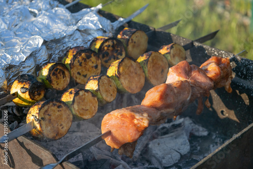 Delicious shish kebab and zucchini grilling on skewers over hot coals in a backyard grill. Meat and vegetables cooking outdoors during a sunny weekend picnic, preparing a tasty meal for family