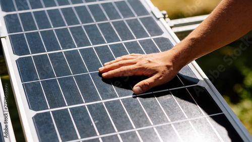 Closeup view of hand touching solar panel in agrivoltaics system with crops below