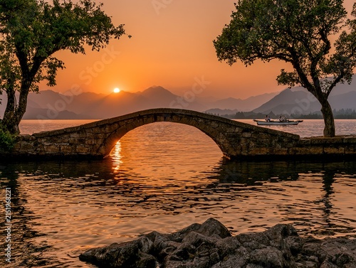 Golden sunset contrasting with dark mountain shadows, layered composition of bridge boat and trees in eastern landscape