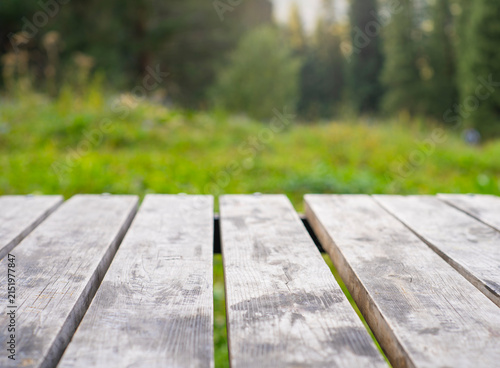 Empty wooden table surface against blurred mountain forest background with bright summer sunshine and copy space