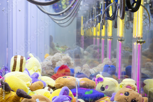 Metallic claw arm with articulated joints and industrial finish hovers in ready position; vivid arcade backdrop and soft prizes create contrast between mechanical precision and playful reward