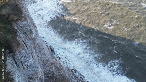 Drone aerial top down static shot of ocean waves crashing against white cliffs