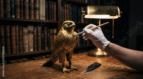 Gloved hand brushing golden falcon sculpture for antique artifact restoration and museum curation appraisal.