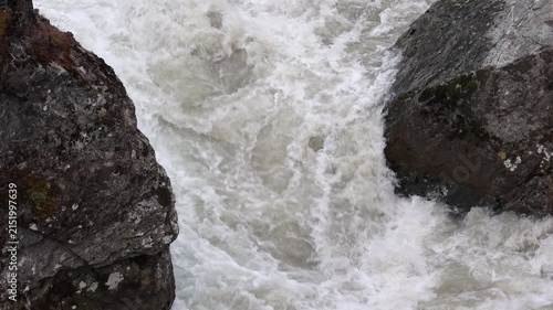 Mountain river water rushing between dark wet mossy rocks